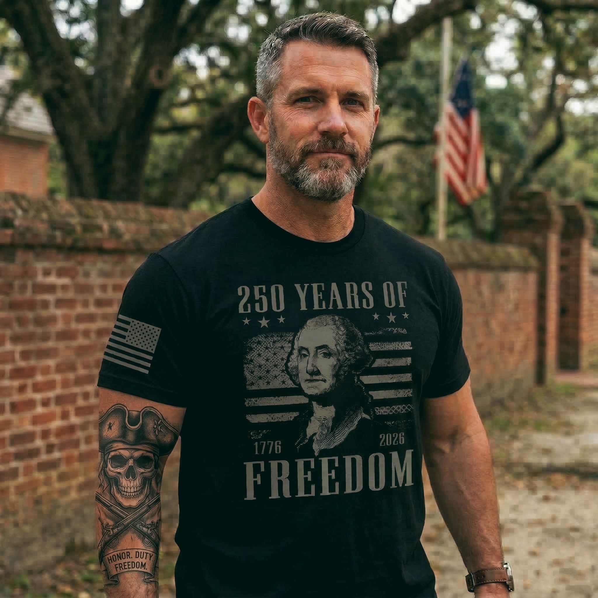 Man wearing a black t-shirt with '250 Years of Freedom' design, standing outdoors with an American flag in the background.